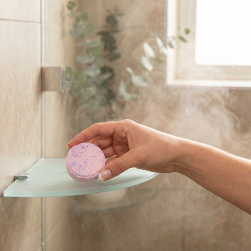 Person placing an aroma shower steamer on a shower shelf