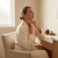 Person applying a silicone neck care patch while seated at a vanity